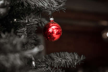 Red, round Christmas tree ornament shines against black & white background.の写真素材