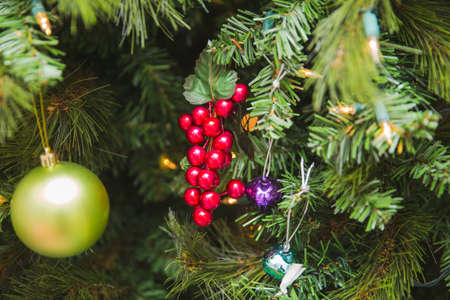 Decorative red Holly berries near other ornaments on a Christmas tree.の写真素材