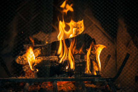 Logs burn inside a fireplace. Metal protective screen in view.の写真素材