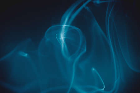 Smoke clouds swirling in blue light against a dark background.の写真素材