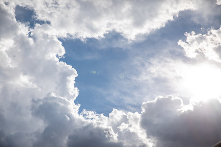 Fluffy white and gray storm clouds gather around a bright sun before a rain storm.の写真素材