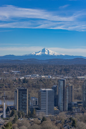 Snow covers Mount Hood behind Portland. The sky is clear and blue, and the mountains are covered in...