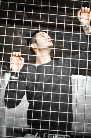 Handsome young man caged behind metal or steel netの写真素材