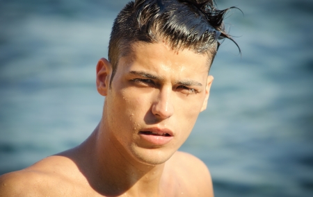 Attractive young man in the sea getting out of water with wet hair, looking in cameraの写真素材