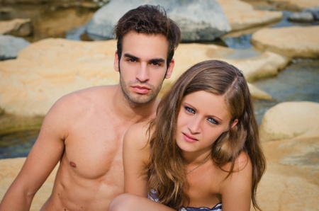 Young romantic couple of boyfriend and girlfriend in swimsuit on rocks by the waterの写真素材