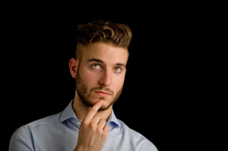 Attractive young man looking up, thinking, isolated on black backgroundの写真素材