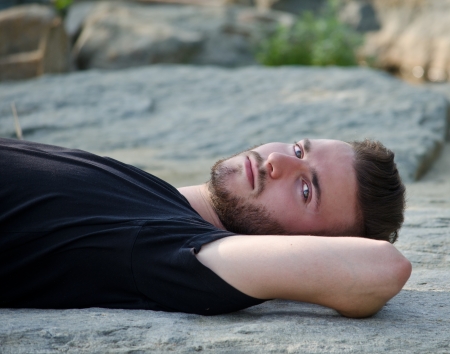 Handsome young man lying on his back on a rock, looking in camera, outdoorsの写真素材