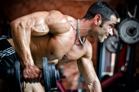 Muscular male bodybuilder working out in gym, exercising triceps leaning on a benchの写真素材