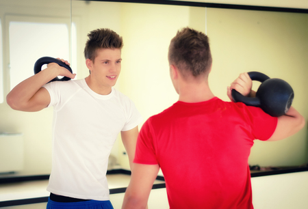 Two handsome young men in gym exercising with kettlebells, smilingの写真素材
