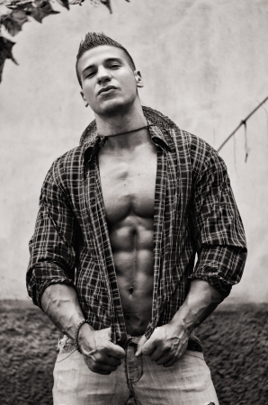 Handsome, muscular young man with open shirt, jeans and straw hat outdoors, black and white shotの写真素材