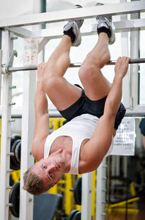 Young man in gym working out, exercising abs by hanging upside-down