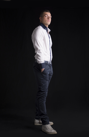 Full body shot of attractive young man with white shirt, hands in pockets, on dark の写真素材