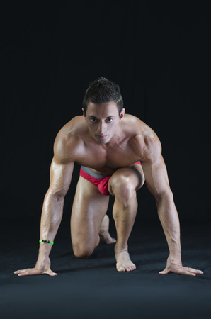 Handsome young muscular man shirtless ready to sprint and run. On dark backgroundの写真素材
