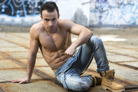 Muscular shirtless young man in abandoned warehouse sitting, looking at cameraのeditorial素材