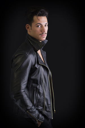 Attractive young man with leather jacket, on dark background, looking at cameraの写真素材