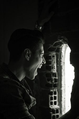 Young man indoor screaming out through hole in the wall, black and white shotの写真素材