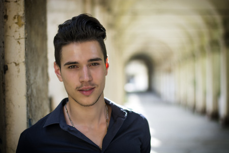 Handsome young man standing outdoors under old colonnade in european town, smilingの写真素材