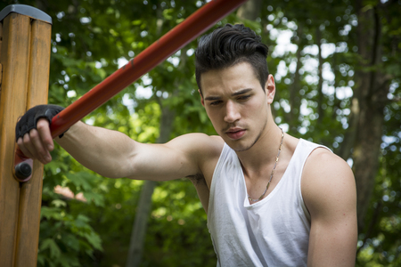 Attractive young man exercising and working out in outdoor gym in city park