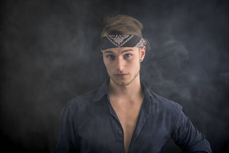 Handsome blond young man wearing bandana, smoke around him, dark backgroundの写真素材