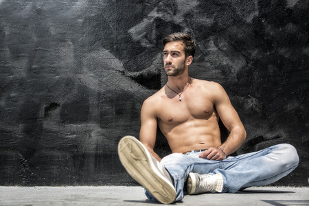 Handsome bearded shirtless young man sitting outdoors in urban environmentの写真素材