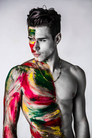 Attractive young man shirtless, skin painted all over with bright holi colors on light backgroundの写真素材