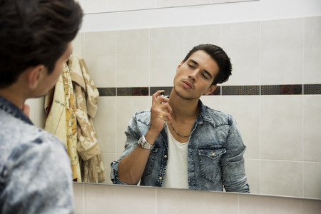 Handsome young man in his home bathroom, spraying cologne or perfume on neckの写真素材