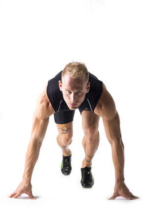 Young blond male runner crouching in the starting position at the beginning of a race or timed...