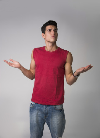 Handsome unsure, doubtful young man shrugging with arms openHandsome unsure, doubtful young man shrugging with arms open, looking awayの写真素材