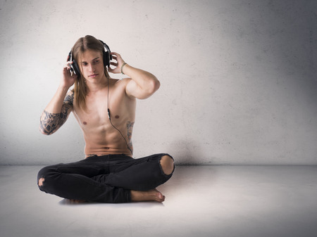 Muscular young man shirtless, sitting and listening to music on headphonesの写真素材