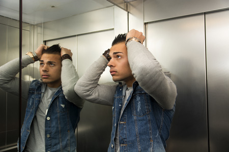 Scared young man desperate in stuck elevator with hands on his headの写真素材