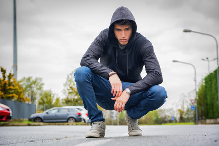 Attractive young man with hoodie and baseball cap in city street, looking at cameraの写真素材