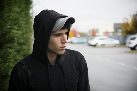 Attractive young man with hoodie and baseball cap in city street, sad or thinkingの写真素材