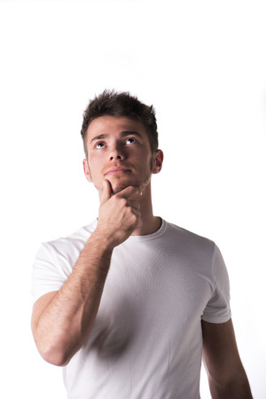 Attractive young man in white shirt, thinking with hand on his chin, isolated on white backgroundの写真素材