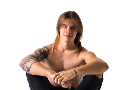 Attractive young man with long hair shirtless, sitting, looking at camera, isolated on whiteの写真素材