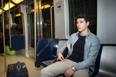 Young man sitting in subway train commuting to work looking awayの写真素材