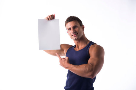 Handsome athletic muscular man pointing to a blank white sign that he is holding up in his hand with a warm friendly smile, isolated on whiteの写真素材