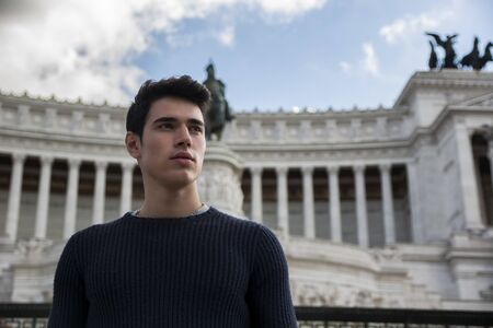 Attractive young man in Rome, Italy, in front of Vittoriano monument standing, looking away