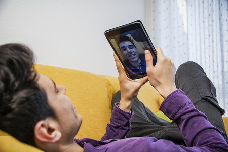Sexy handsome young man sitting indoors  taking selfie or video chatting with tablet PC smiling for...