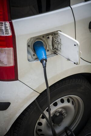 Charging an electric car at a roadside urban charging station showing a close up of the attached connector and cable in a green energy concept Charging an electric car at a roadside urban charging station showing a close up of the attached connector and cable in a green energy concept