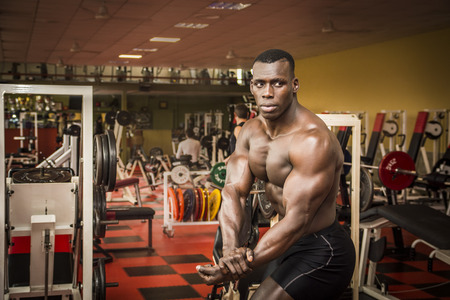 Attractive hunky black male bodybuilder doing bodybuilding pose in gymの写真素材