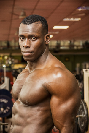Attractive hunky black male bodybuilder doing bodybuilding pose in gymの写真素材