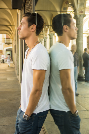 Handsome young man and his reflection in shop window outdoors in town, casually dressedの写真素材