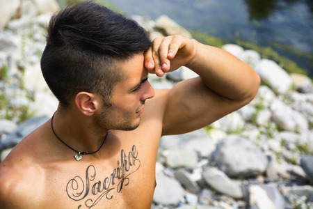 Attractive muscular shirtless young man in nature shielding eyes from sun with his handの写真素材