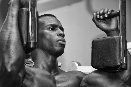 Hunky muscular black bodybuilder working out in gym, exercising pecs on machine