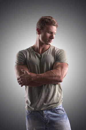 Fit handsome young man standing confident in casual clothes, looking down, arms crossedの写真素材