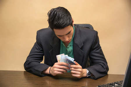 Close up Serious Young Businessman, Sitting at his Worktable, Counting Cash on Hand Seriously.の写真素材