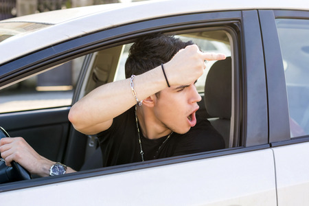 Handsome Young Man Driving a Car and showing the middle finger to someone behind himの写真素材