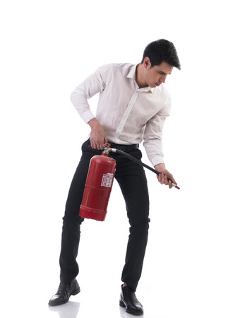 Young Man Wearing Business Wear Standing in Studio Holding Fire Extinguisher and Posing as if Using it on Fireの写真素材