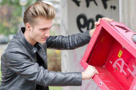 Handsome young male vandal breaking public property, pulling down metal object
