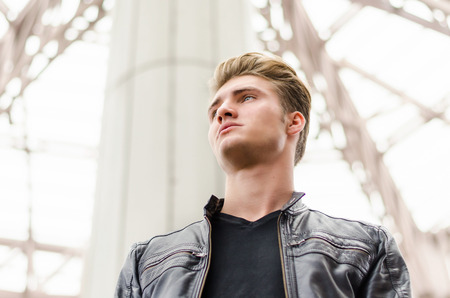 Attractive blond young man in city environment, looking away, shot from belowの写真素材